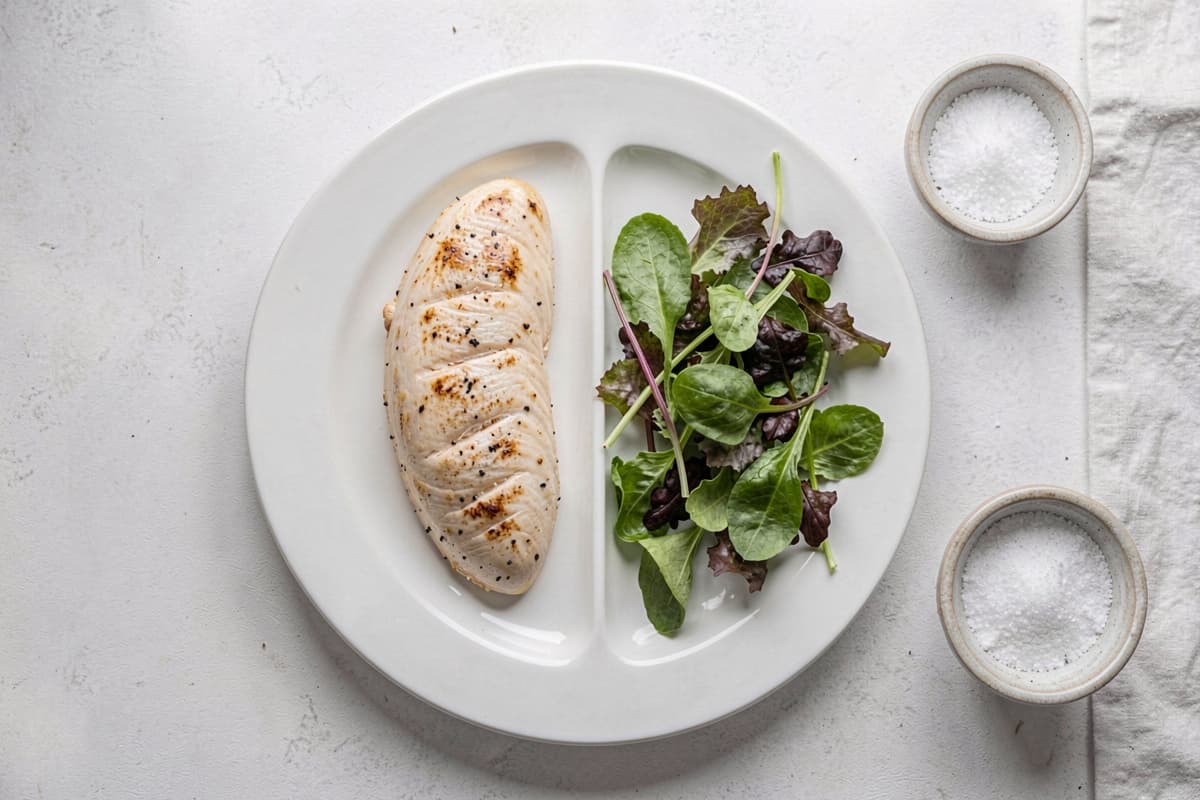Lean chicken breast and salad next to a dish of salt — visual representing common carnivore diet mistakes