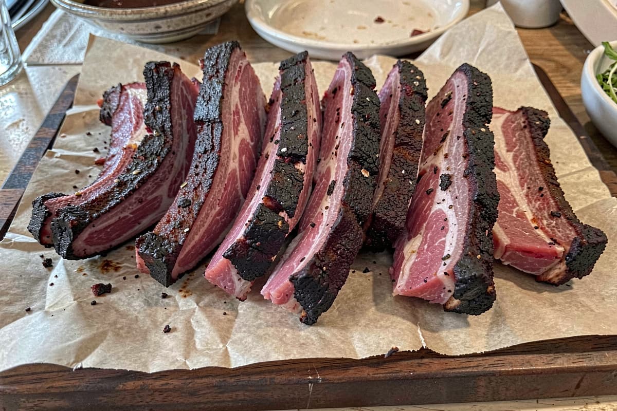 Rack of 3-2-1 baby back pork ribs on butcher paper, dark mahogany bark, sliced between bones showing tender pink-edged meat