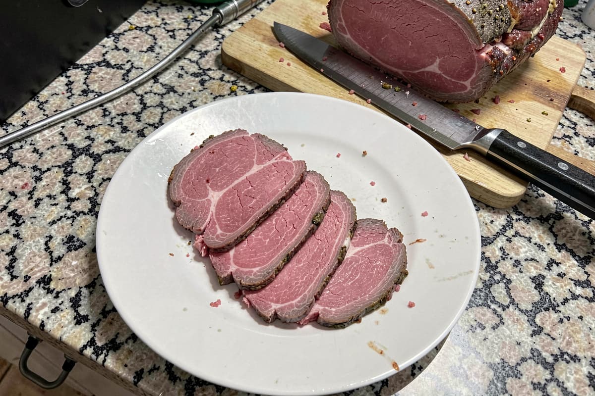 Thinly sliced bottom round roast on a wooden carving board, rosy medium-rare slices, butter pat melting on top