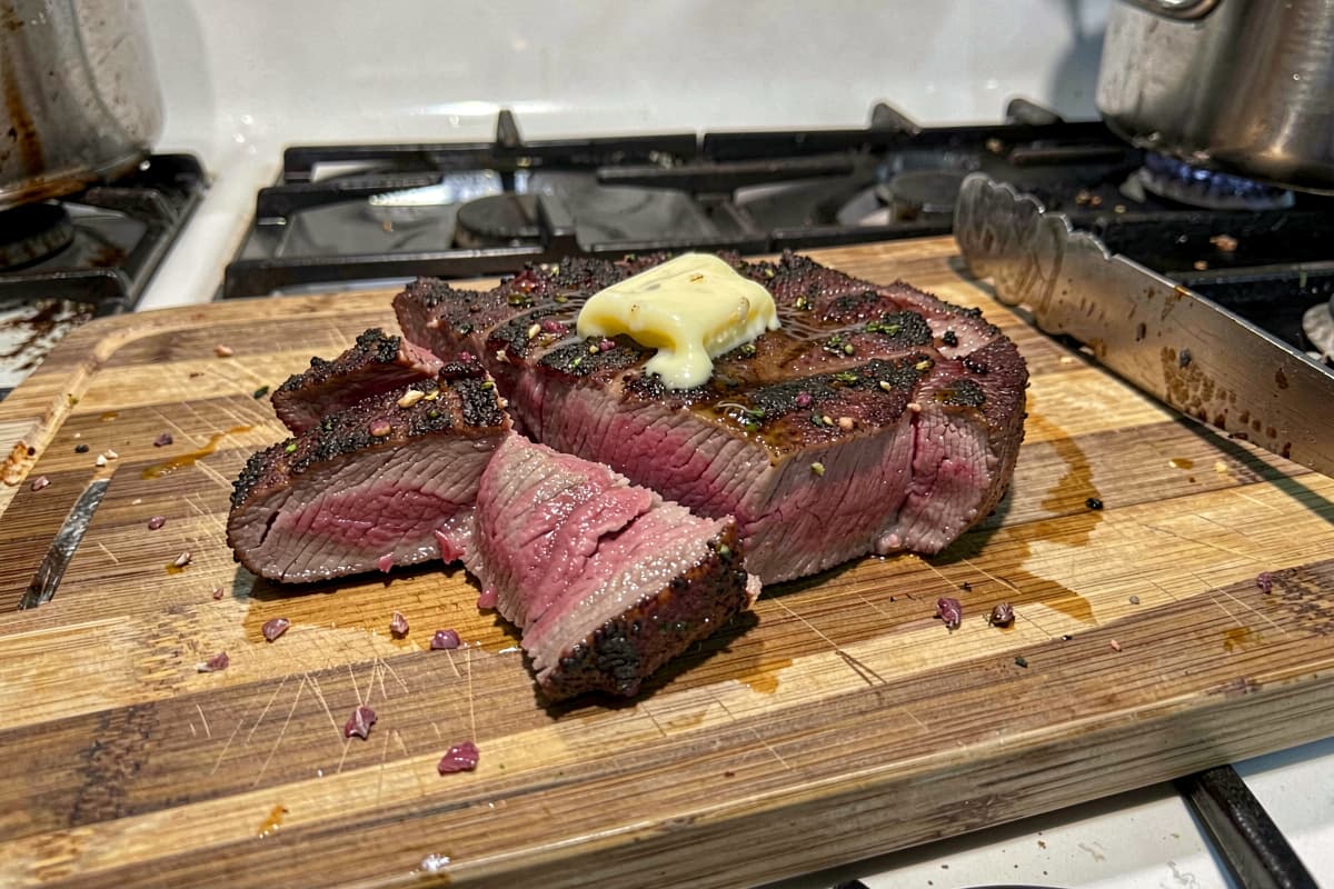 Sliced butter-basted ribeye steak with deep brown crust and medium-rare pink interior on dark slate
