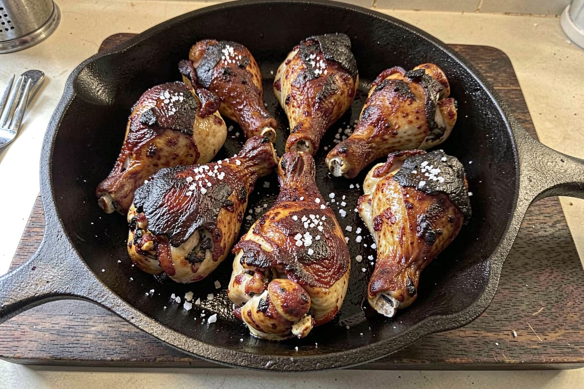 Eight bone-in chicken thighs in a cast iron skillet, deep mahogany shattering crispy skin tight against the meat, glistening with rendered fat, scattered salt