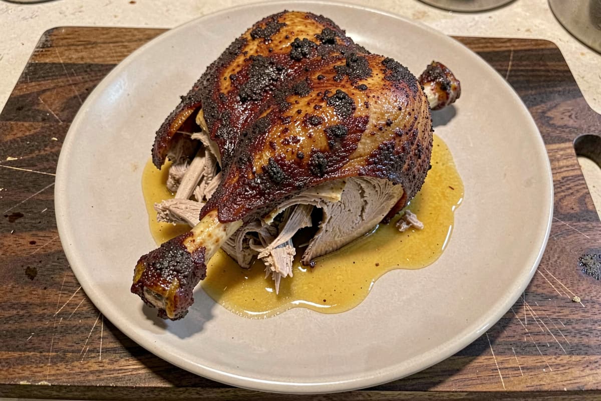 Duck confit leg on a wooden plate, deep mahogany crispy skin, fork-tender meat falling off the bone, golden duck fat pooled around the leg