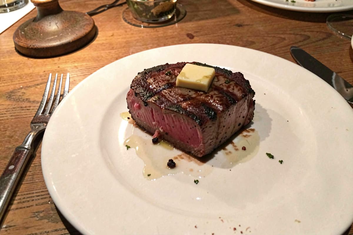 Pan-seared filet mignon medallion on a white plate with deep rosy interior, butter pat on top, coarse salt scattered
