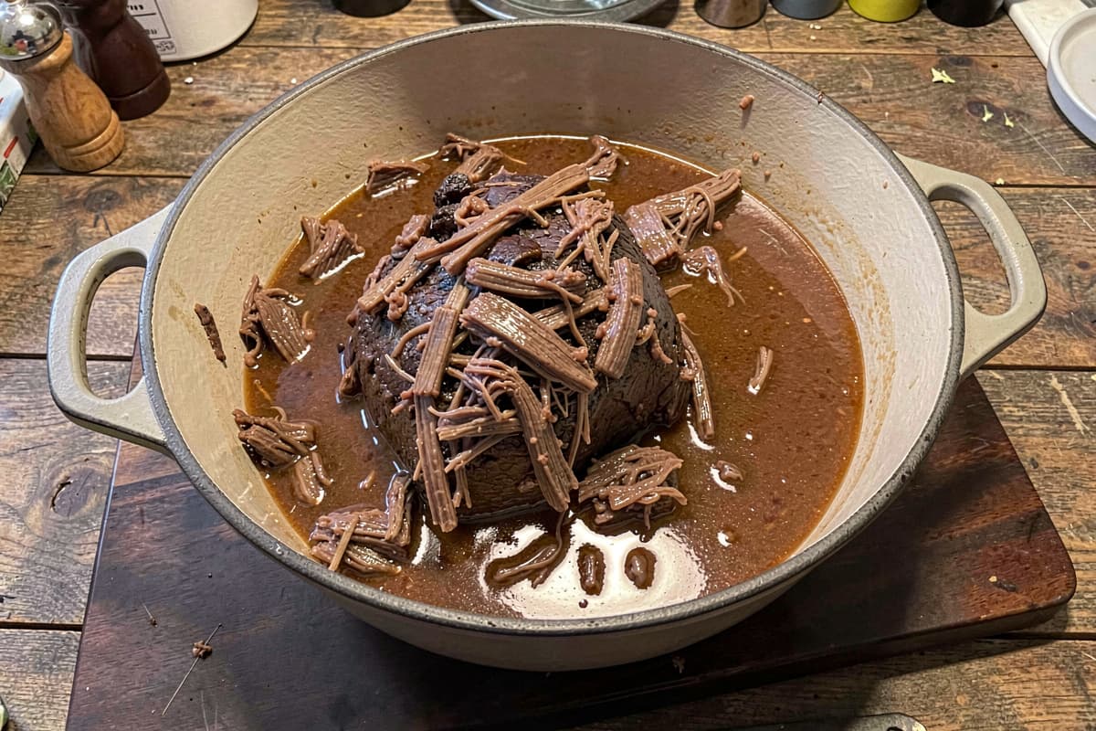 Slow-cooked beef pot roast in a Dutch oven, fork-shredded meat in glossy braising liquid — carnivore meal-prep staple