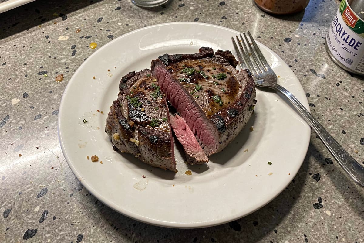 Pan-seared ranch steak on a wooden cutting board, sliced to show medium-rare interior, butter pat melting on top