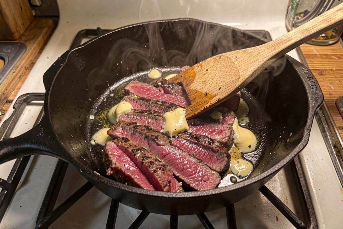 Thinly sliced skirt steak across the grain on a wooden cutting board, deep brown crust, rosy medium-rare interior, salt scattered