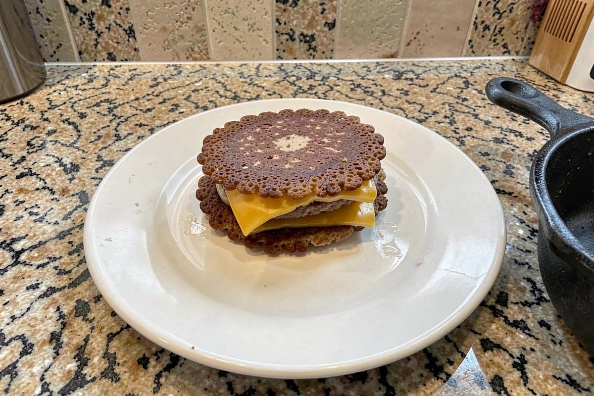 Two crispy-edged carnivore smash burger patties with melted cheddar stacked on a white ceramic plate
