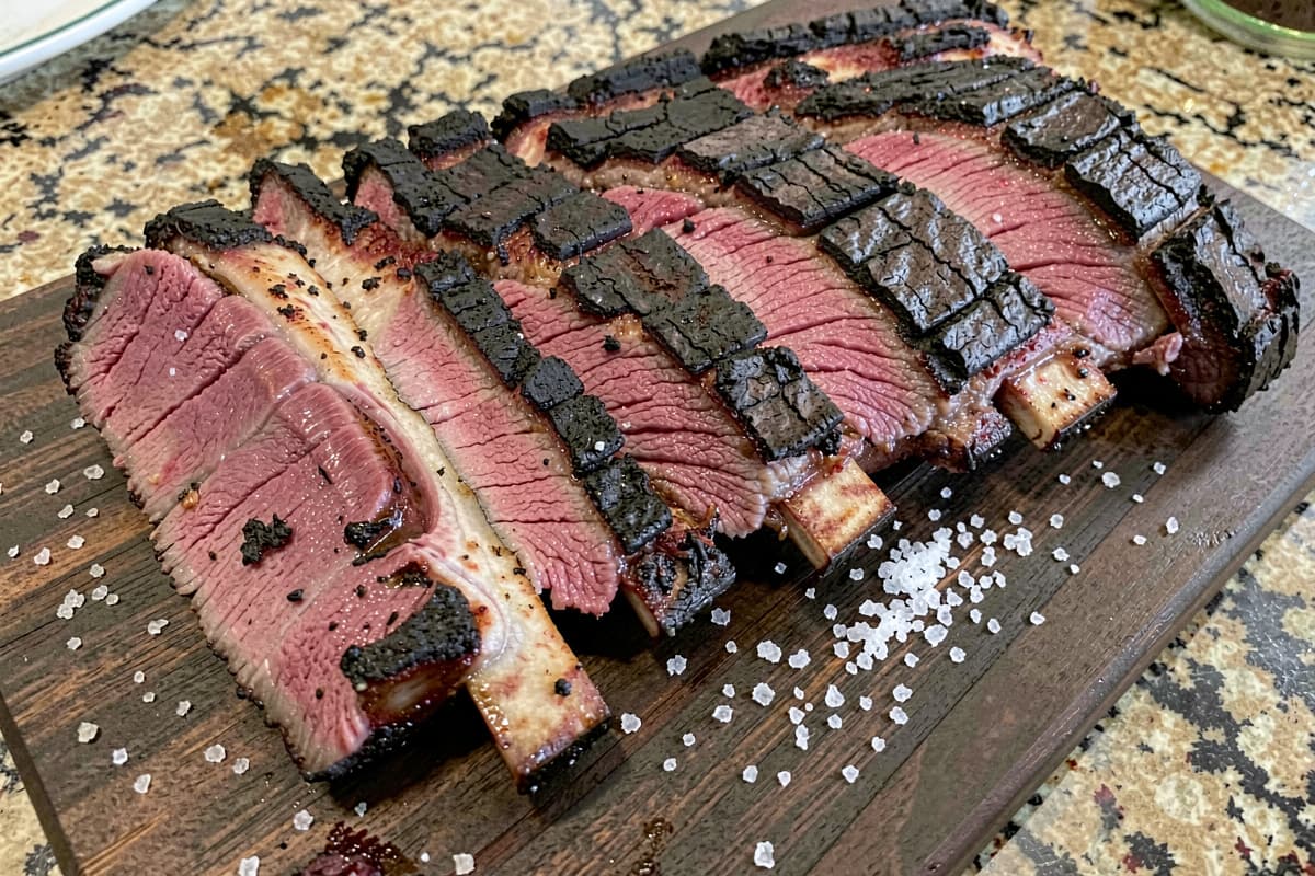 Rack of no-wrap smoked baby back ribs on a wooden board, near-black mahogany bark, sliced between bones showing deep pink smoke ring
