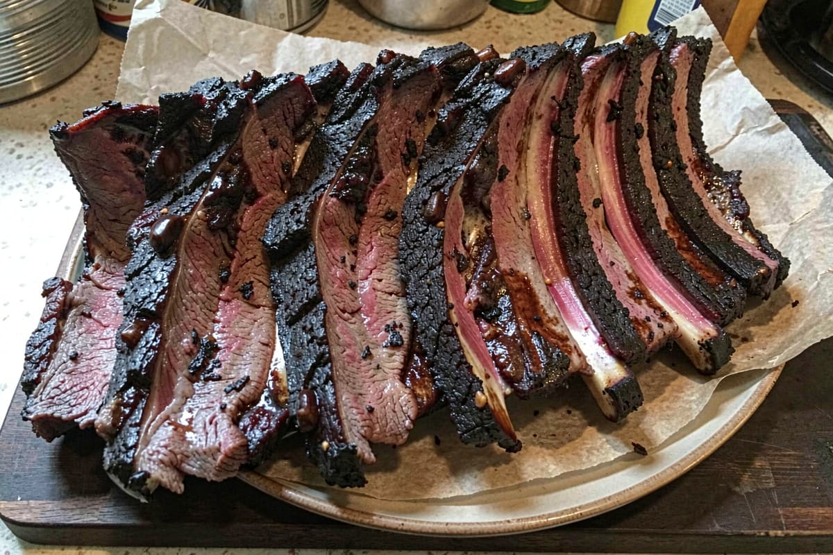 Massive rack of smoked beef back ribs on butcher paper, dark mahogany bark, meat curling away from the bones, prominent pink smoke ring