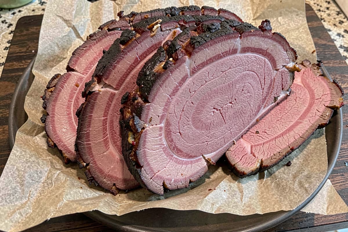 Sliced smoked beef brisket on butcher paper, deep mahogany bark, prominent pink smoke ring under the surface, juicy slices fanned out