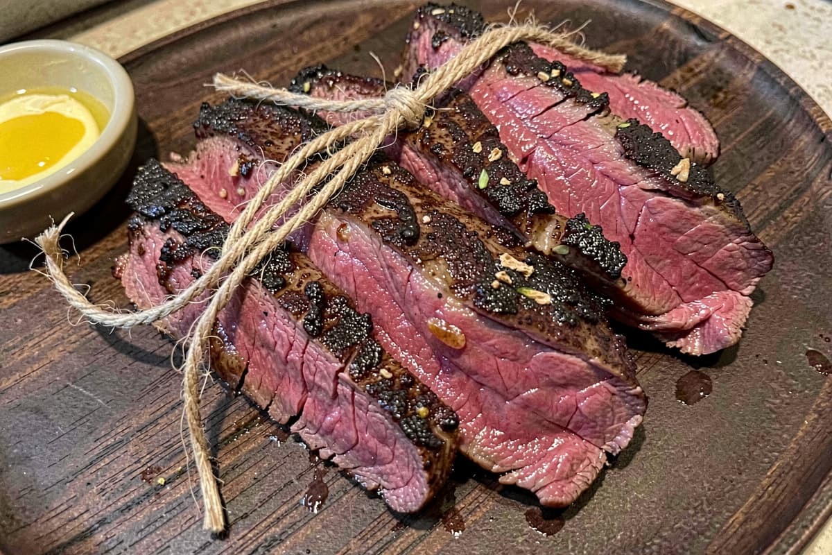 Sliced smoked beef tenderloin medallions on a wooden board, dark seared crust, deep pink medium-rare interior, butcher twine and butter visible nearby