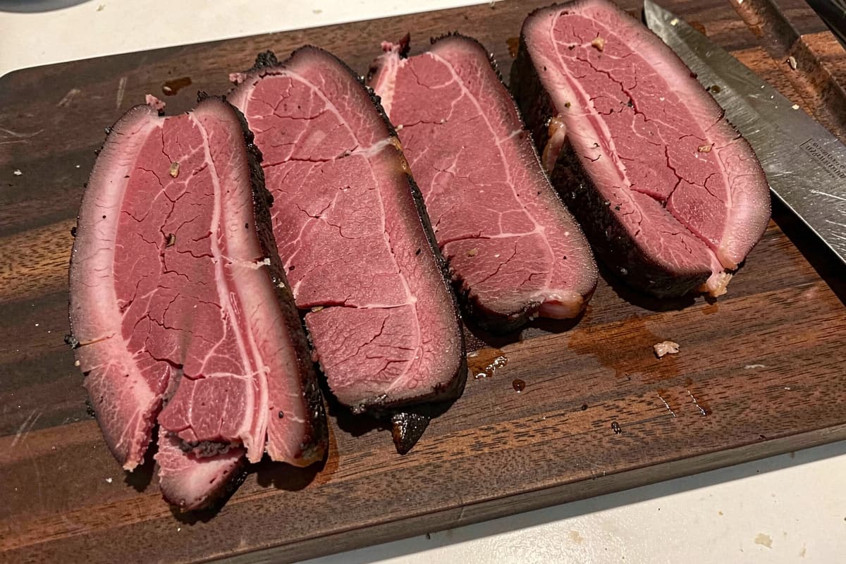 Sliced smoked corned beef on a wooden board, deep red interior with prominent pink smoke ring under a dark crust, thin slices fanned out