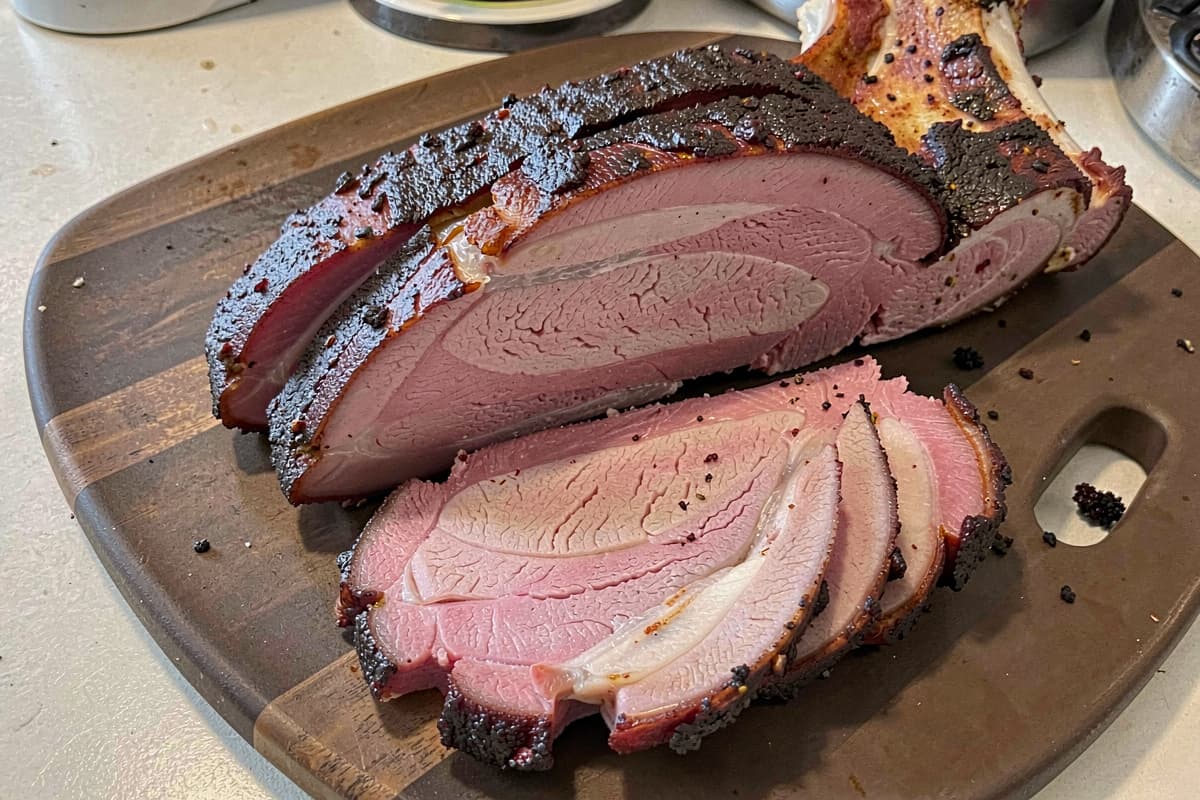 Sliced smoked pork butt on a wooden board, dark crispy bark on top, juicy pink-edged interior, slices fanned out showing texture