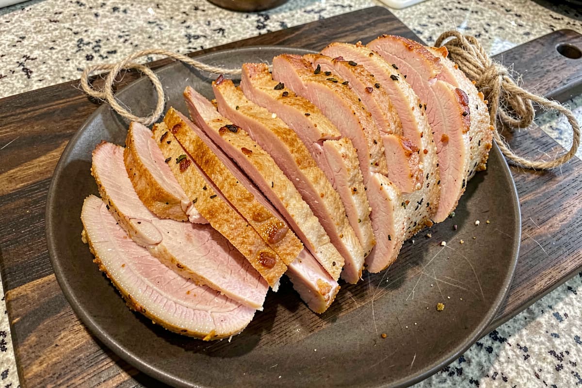 Sliced smoked pork loin on a wooden board, light golden crust, faint pink interior, slabs fanned out showing even color edge to edge
