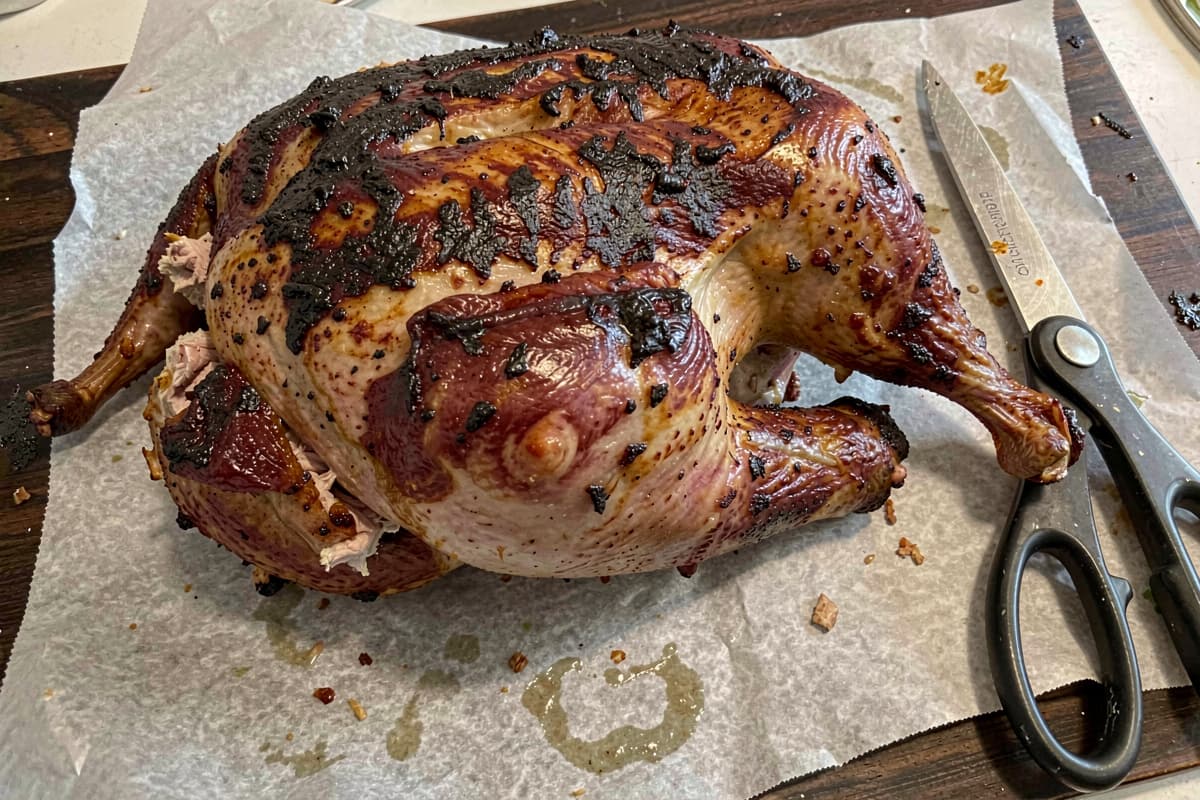 Spatchcocked smoked turkey lying flat on butcher paper, mahogany skin, juicy meat visible at the leg joint, kitchen shears resting nearby