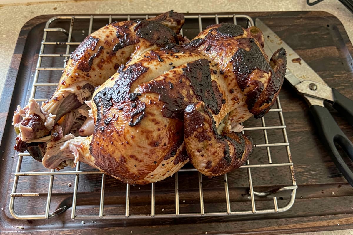 Spatchcocked roast chicken lying flat on a wire rack, mahogany-brown crispy skin, juicy meat visible at the leg joint, kitchen shears resting nearby