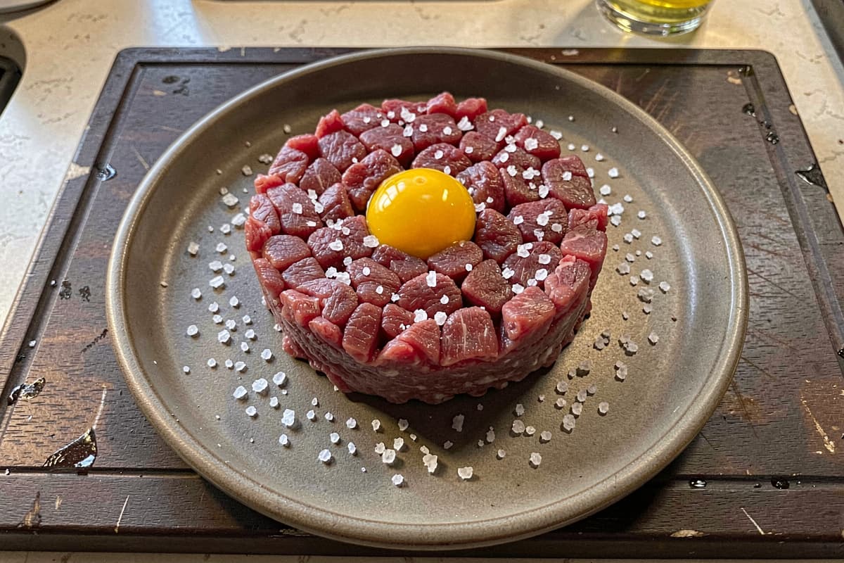 Carnivore steak tartare on a chilled plate, finely chopped raw beef formed into a 4-inch round, single egg yolk in the center well, salt scattered around the rim
