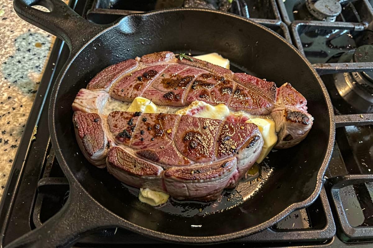Pan-seared top blade steak on a wooden cutting board with the connective tissue band visible down the middle, sliced halves on either side