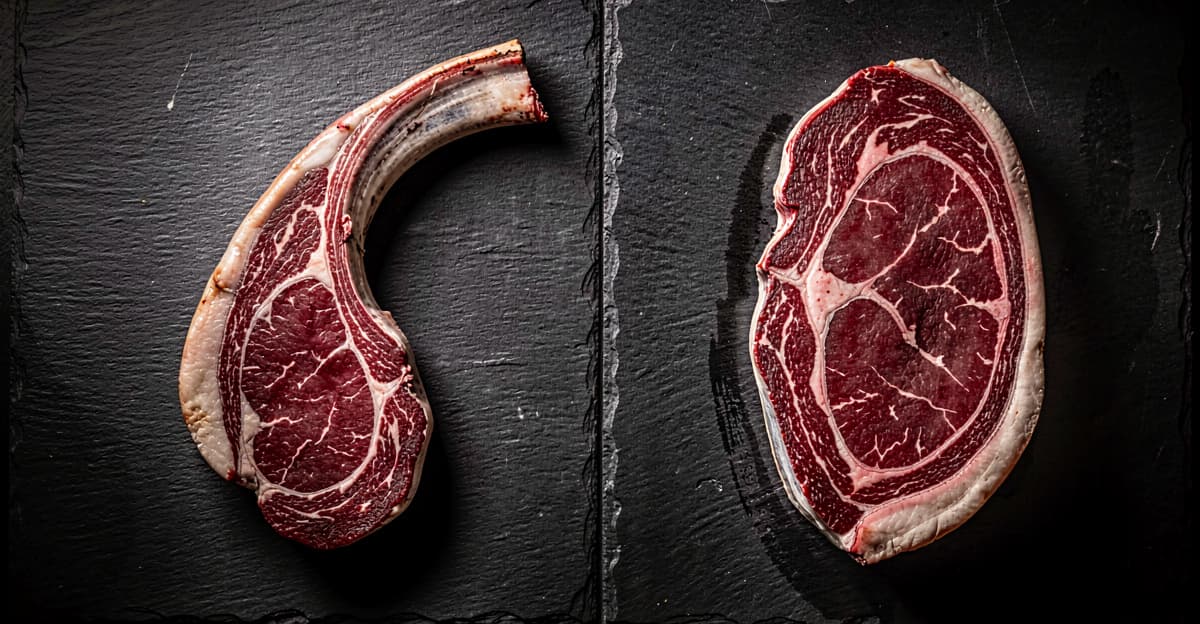 Tomahawk steak with long bone next to boneless ribeye for size comparison